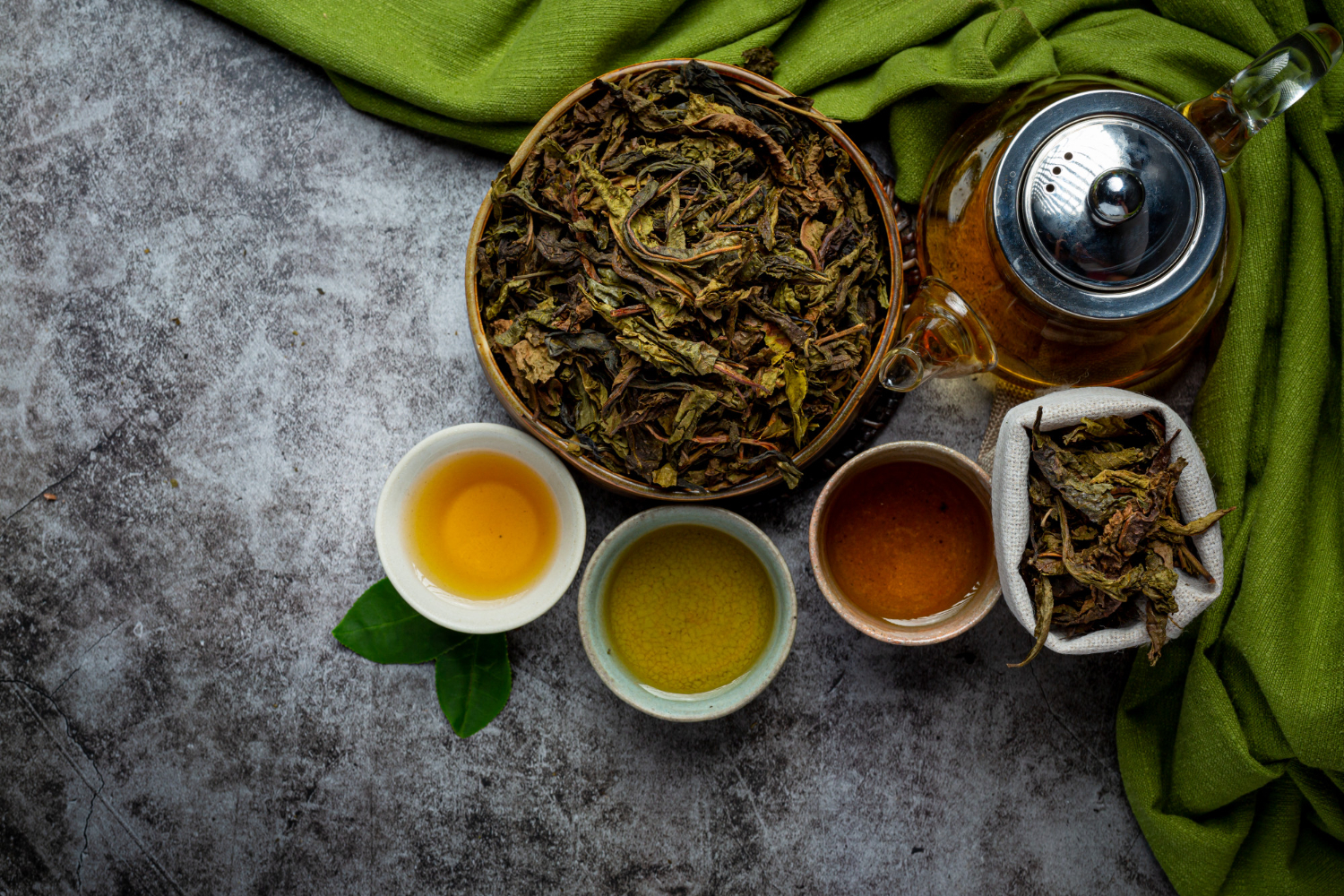 Vue aérienne montrant comment préparer le thé oolong avec trois tasses affichant différents degrés d'oxydation et d'infusion gongfu, accompagnées de feuilles de oolong chinois séchées et infusées.