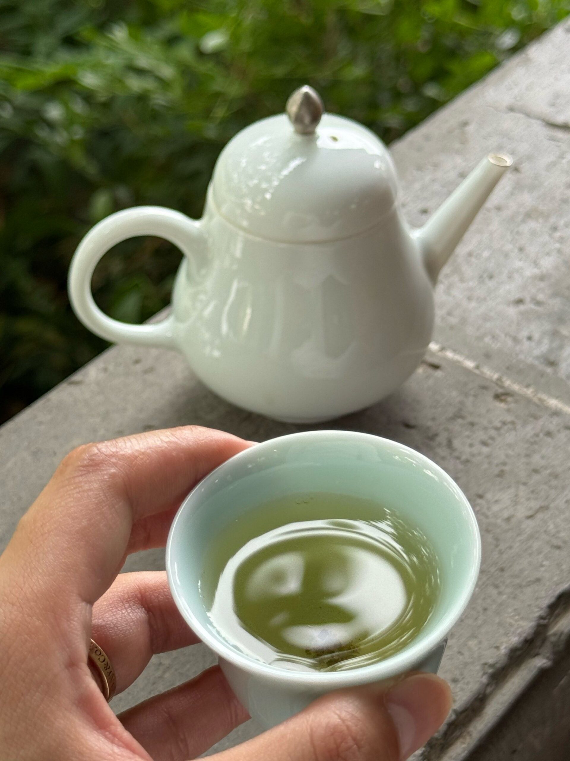 Rituel du thé à Suzhou: main tenant une tasse de thé bilochun et théière blanche, moment de dégustation apaisant.