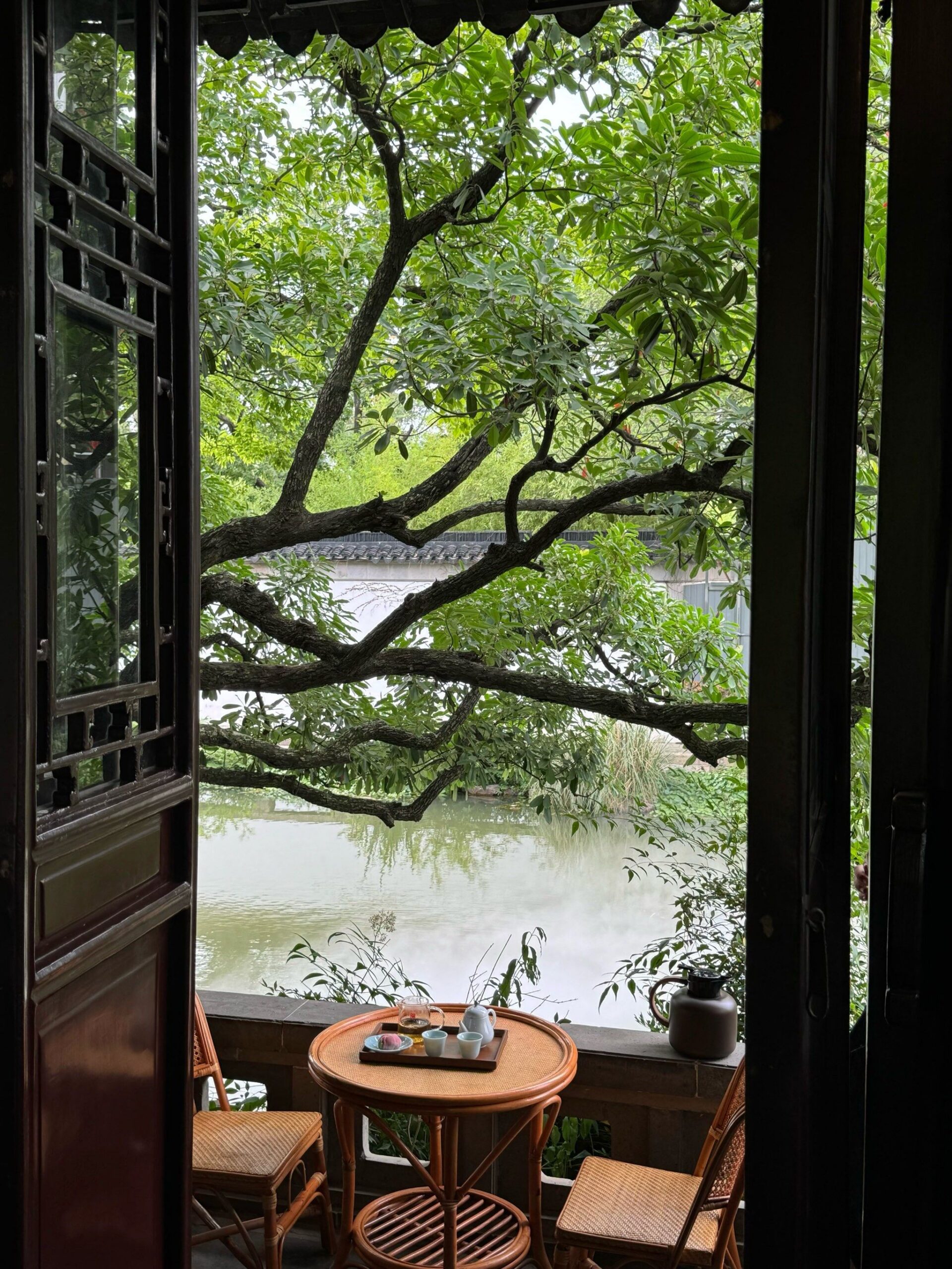 Voyage autour du thé à Suzhou : balcon en Chine avec vue sur l'eau, table en rotin pour un moment de thé paisible en pleine nature.