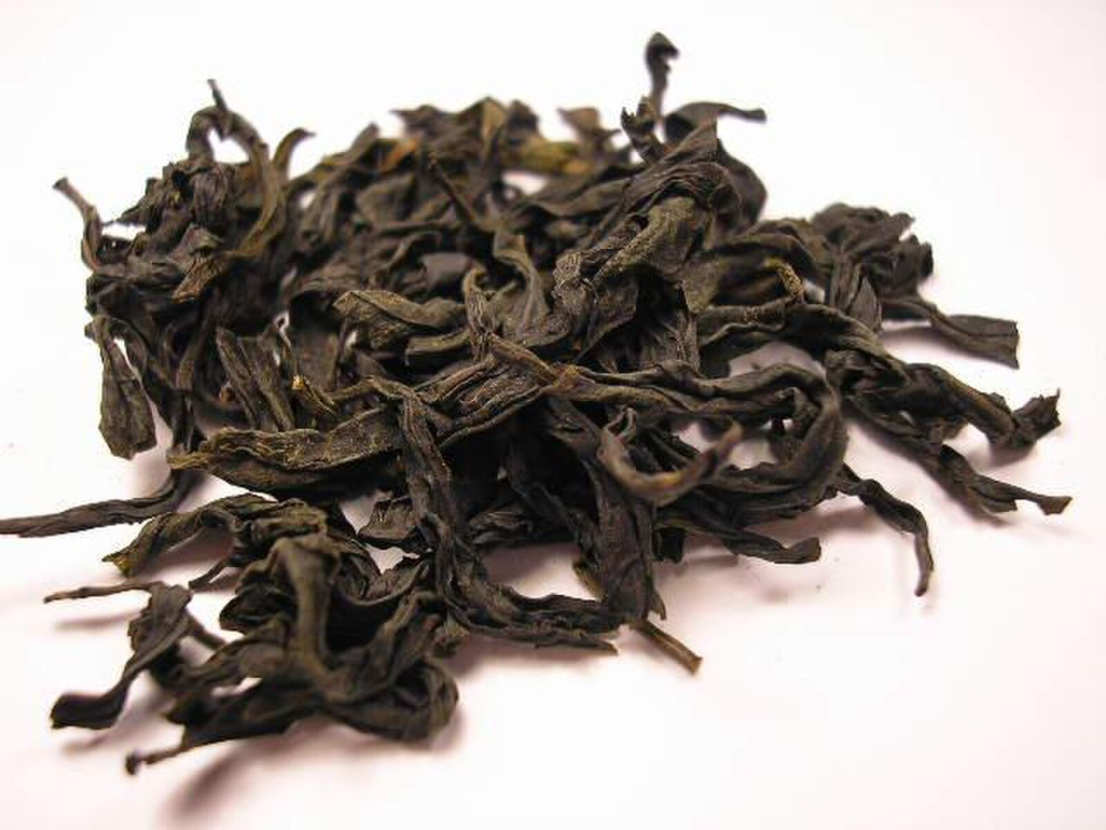 Gros plan sur un tas de grandes feuilles de thé oolong Fo Shou, sombres et roulées, idéal pour un article de blog sur les variétés d'oolong chinois.