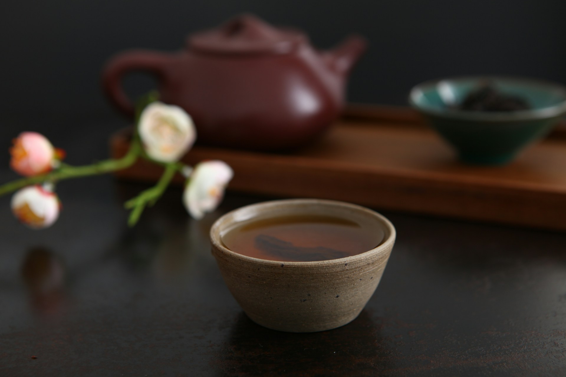 Gros plan sur un thé oolong Da Hong Pao infusé dans une tasse en argile rustique, avec une théière traditionnelle de Yixing et des feuilles de thé en vrac floues en arrière-plan.