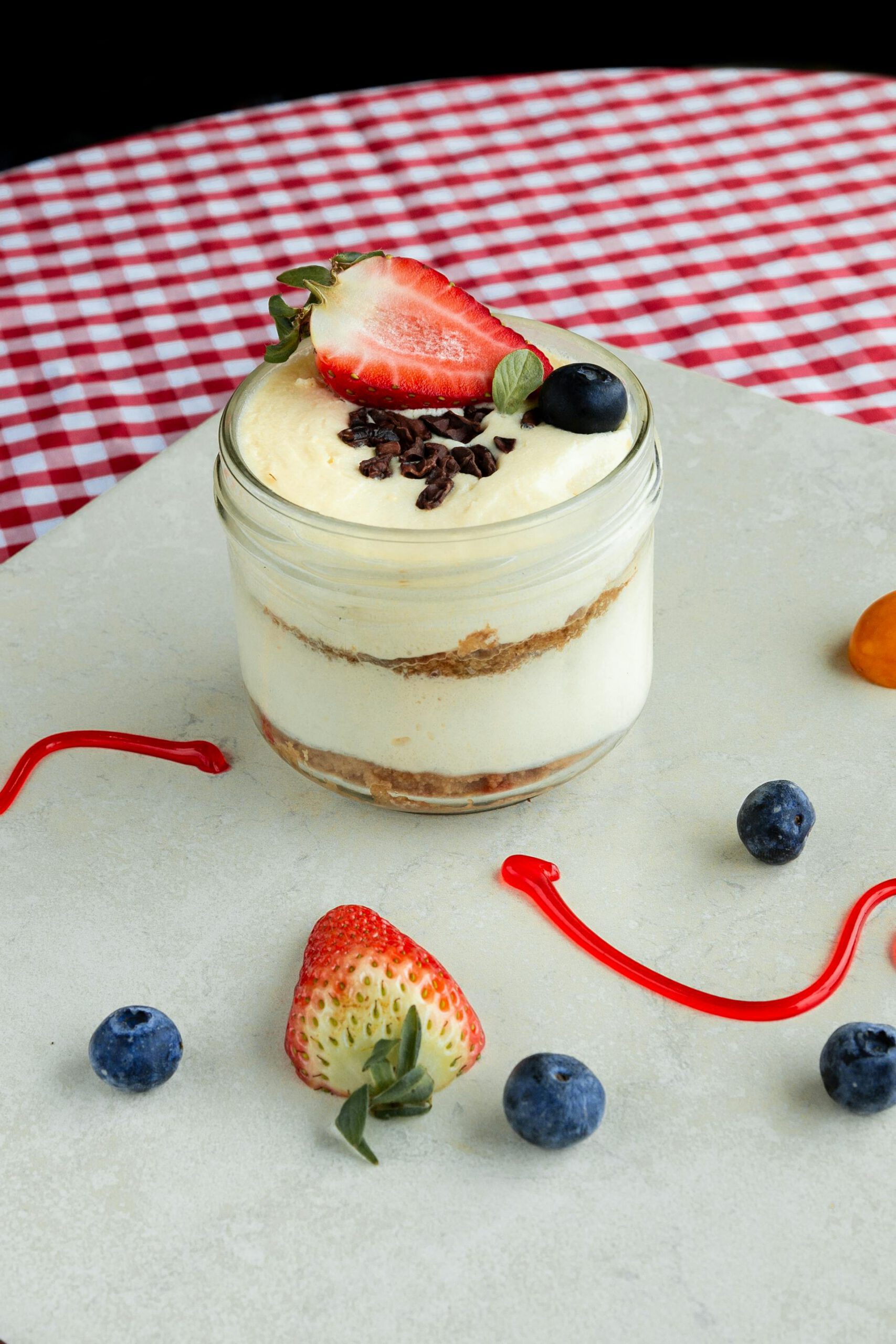 Un dessert en verrine à plusieurs couches, garni d'une fraise fraîche, de myrtilles et de copeaux de chocolat, pour un article de blog sur des recettes de desserts sans cuisson, idéal pour des accords thé et desserts.