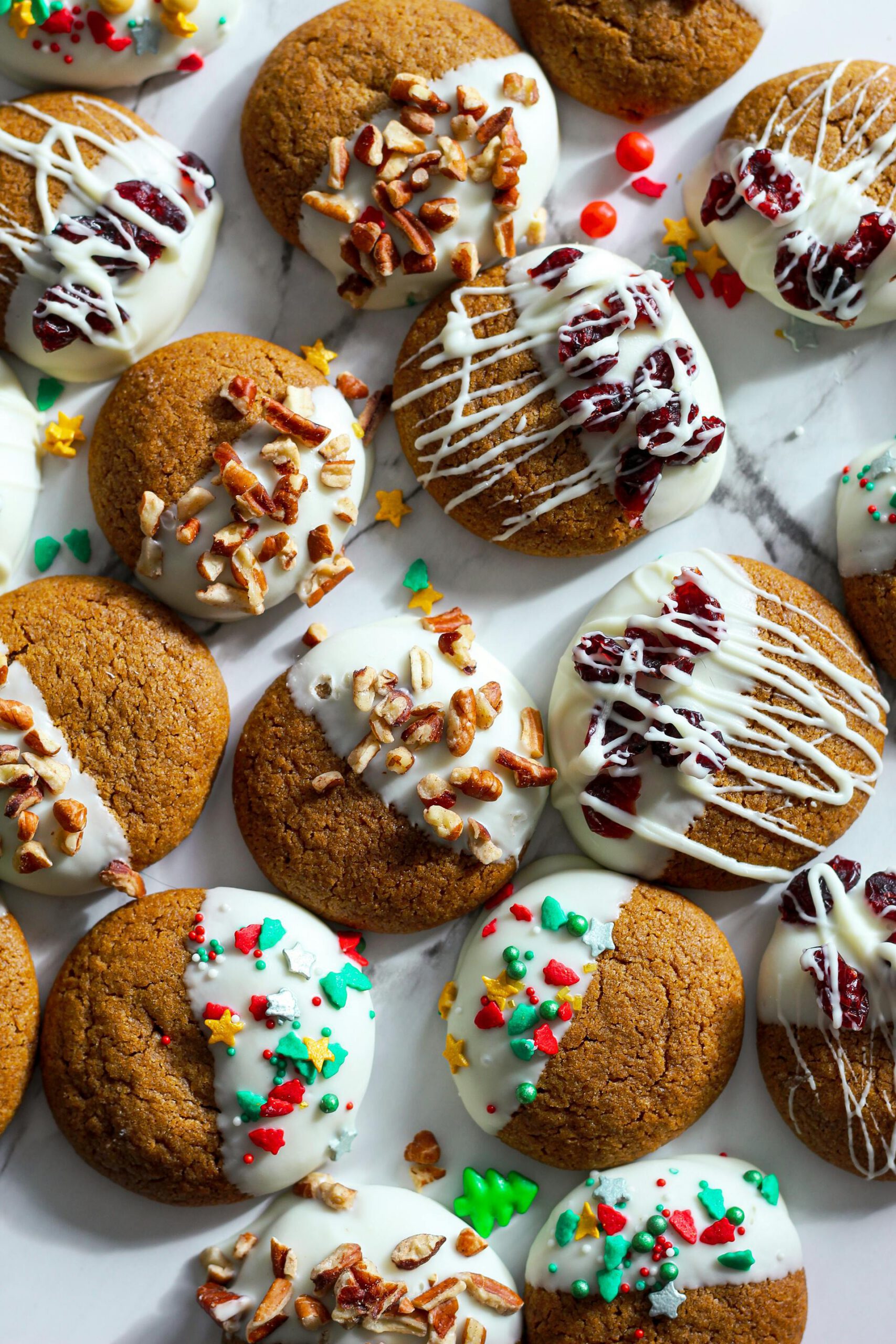 Une variété de biscuits au pain d'épice gourmands, à moitié trempés dans du chocolat blanc et garnis de noix de pécan, de canneberges et de pépites colorées, idéals pour des recettes de pâtisserie des Fêtes.
