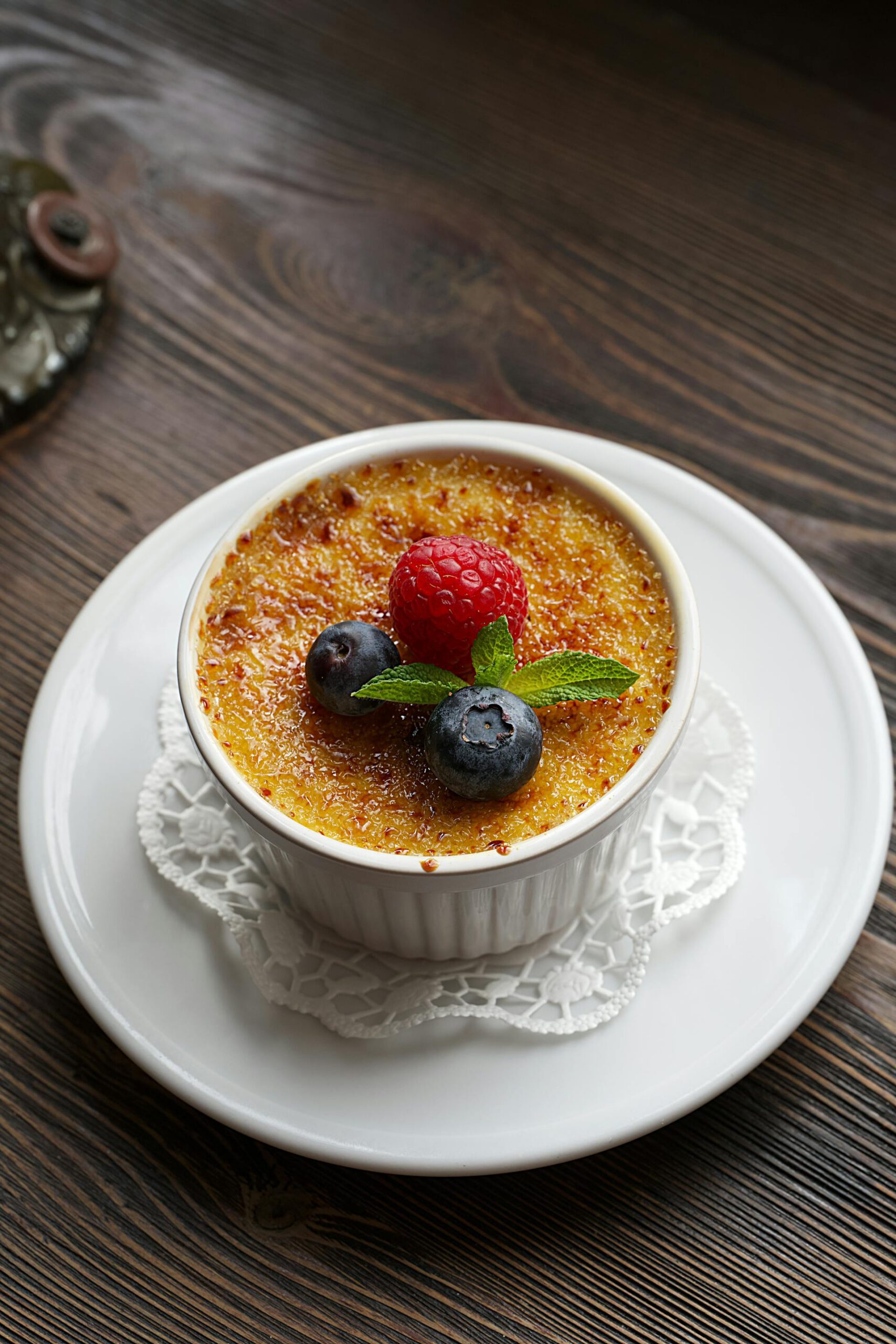 Une crème brûlée classique dans un ramequin en céramique blanc, avec une couche de sucre caramélisé parfaite et garnie de fruits rouges frais, idéale pour un blog de desserts gastronomiques.
