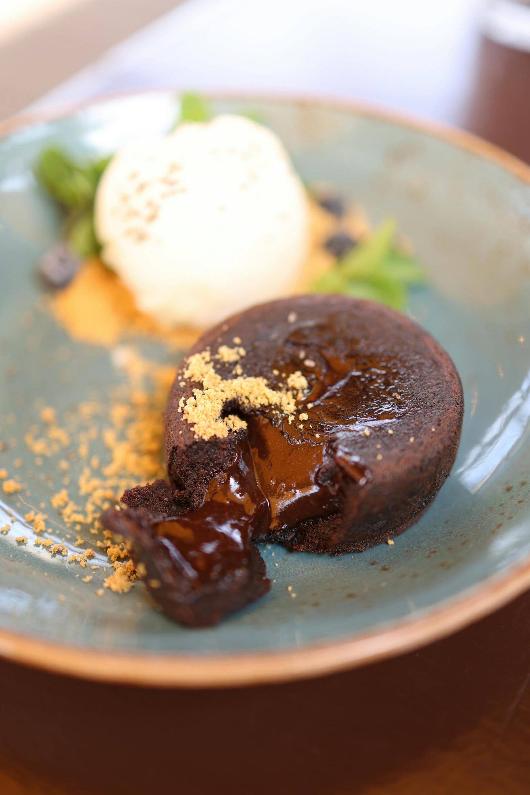 Un moelleux au chocolat décadent et chaud avec un cœur coulant, servi sur une assiette bleue avec une boule de glace à la vanille et parsemé de miettes.