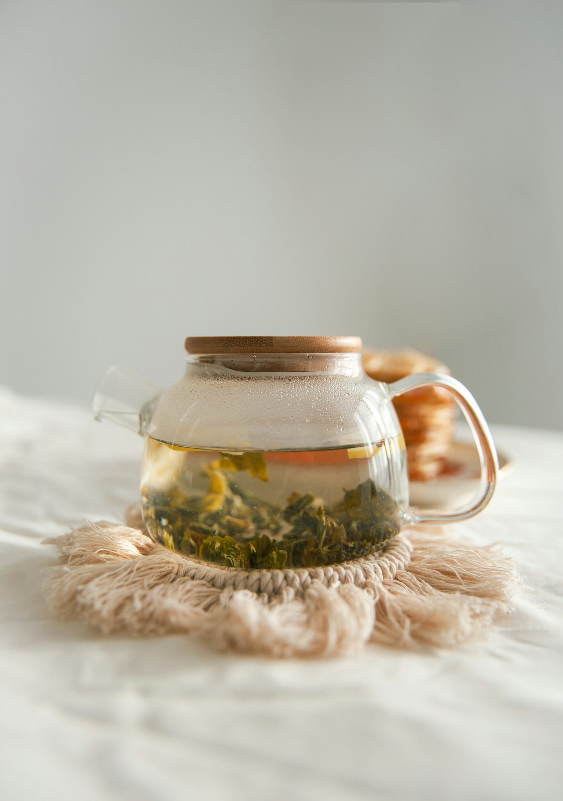 Théière en verre infusant du thé blanc chinois (ou Oolong) sur un napperon en macramé, gros plan sur les feuilles en pleine infusion.