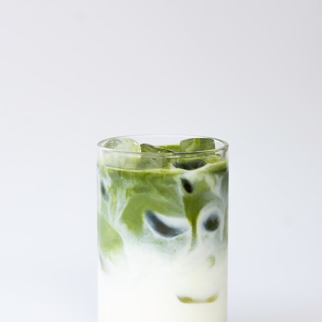 thé matcha latte dans un grand vert avec des glaçons sur un fond gris clair
