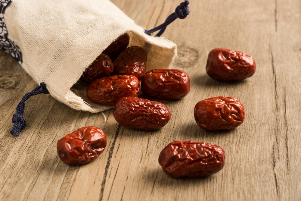 jujubes ou dattes chinoises séchées sortant d'un petit sac un tissu beige et placées sur une tale en bois. Elles sont utilisées pour faire des infusions dans la médecine traditionnelle chinoise.