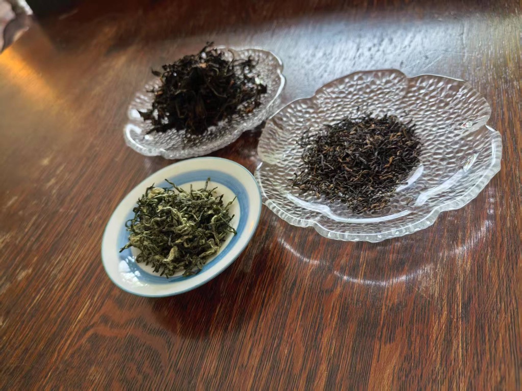 Trois échantillons de thés secs chinois disposés sur des soucoupes sur une table en bois. Le thé vert (ressemblant au Biluochun) est à l'avant, le thé noir est à droite, et un thé sombre ou Oolong très fermenté est à gauche. La photo montre la diversité des thés chinois et leurs différences de couleurs.
