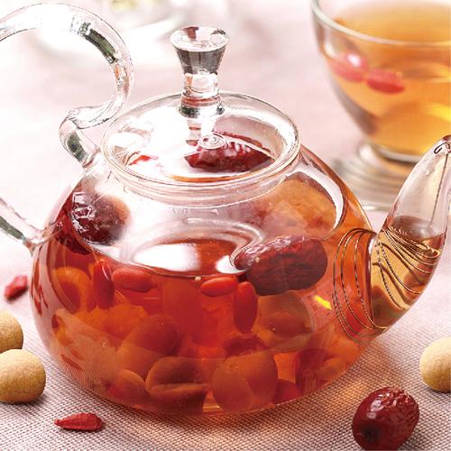 Gros plan sur une théière en verre transparente remplie d'infusions chinoises aux couleurs rouges, contenant des dattes jujube entières et des baies de goji pour leurs bienfaits pour la santé.