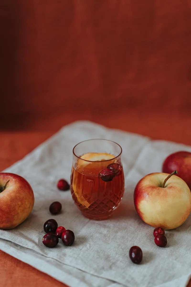 verre transparent contenant l'infusion de chinoise de pomme, jujube et baies de goji. des pommes et des dattes chinoises ou jujubes sont placées sur une nappe blanche autour du verre.