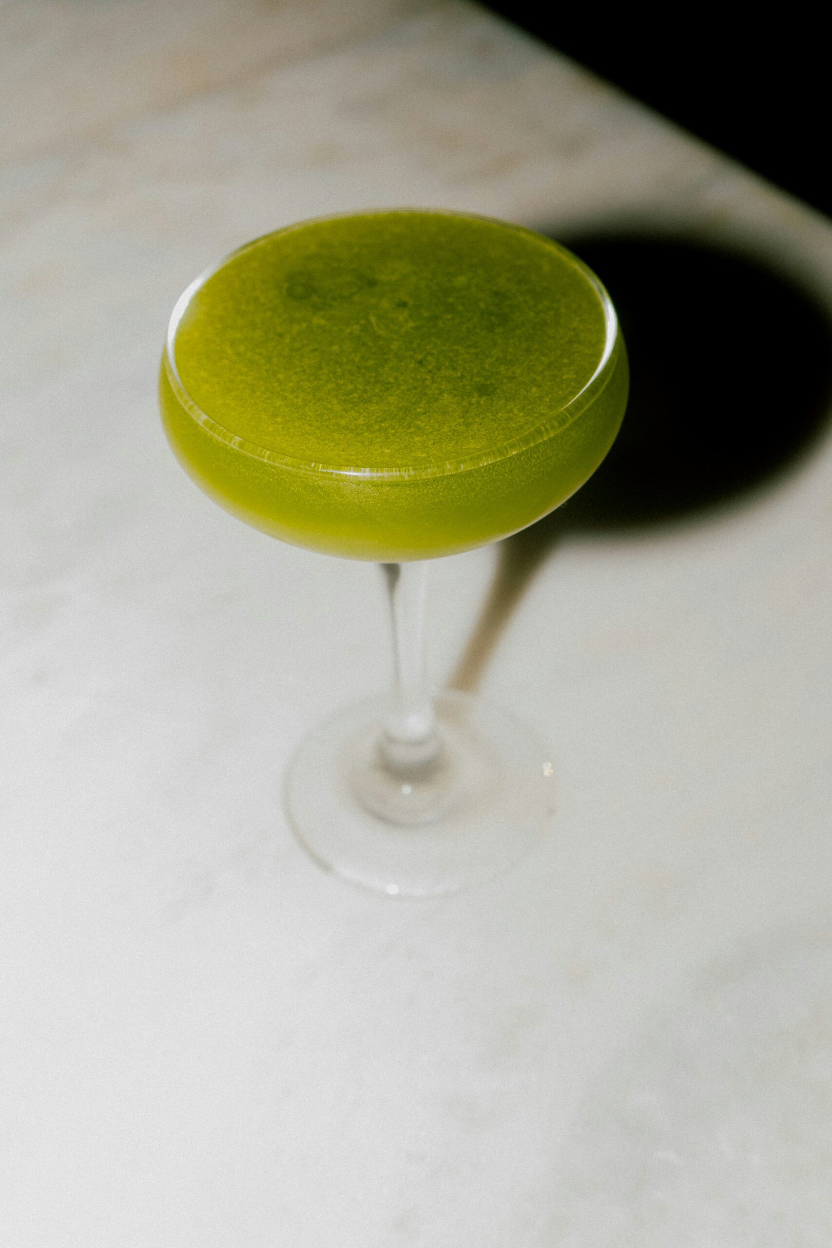 Un cocktail au thé matcha pétillant à la couleur verte éclatante, servi dans un verre highball avec des bulles fines, une tranche de citron frais et une paille réutilisable sur un comptoir de bar moderne.