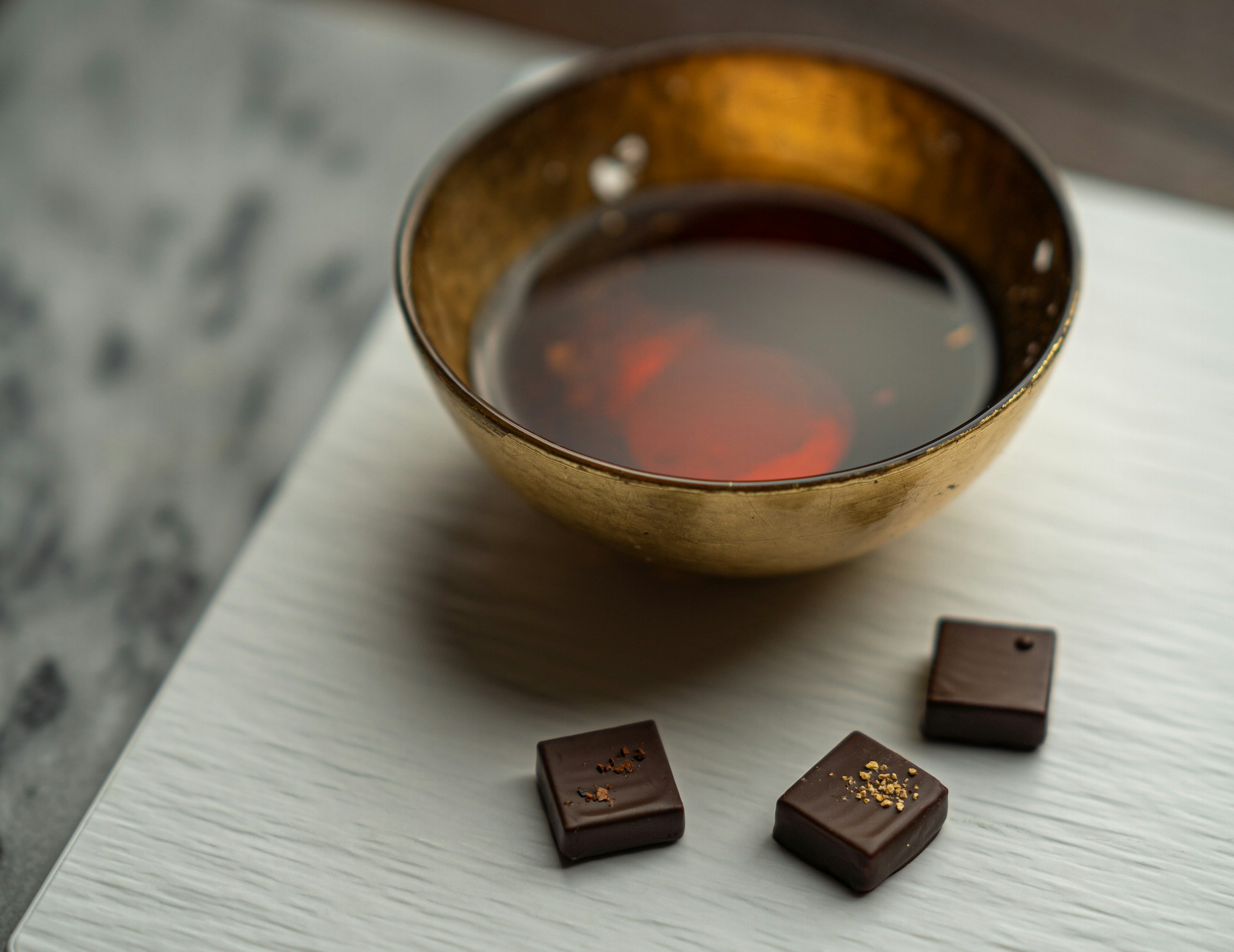 Tasse de thé noir fumant posée à côté de trois chocolats noirs pour une dégustation gourmande. L'image illustre le parfait accord thé et chocolat pour un rituel cosy.