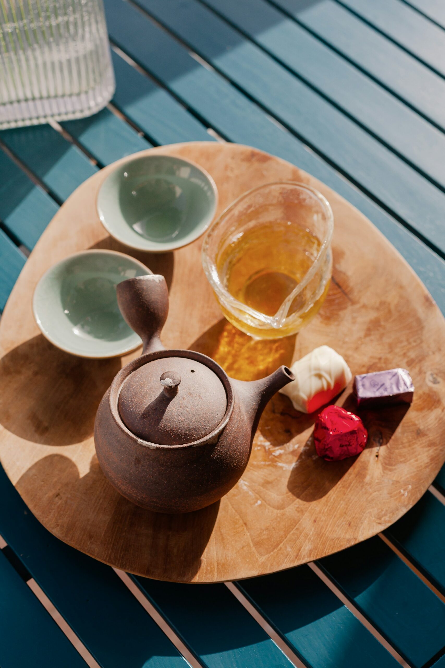Un plateau de dégustation en bois avec une petite théière en terre cuite de style Gongfu Cha et deux tasses miniatures en céramique. À côté de la théière, on voit du thé infusé et quelques chocolats emballés, suggérant un accord thé et dessert. C'est une excellente idée cadeau thé pour les puristes et les amateurs d'art du thé.