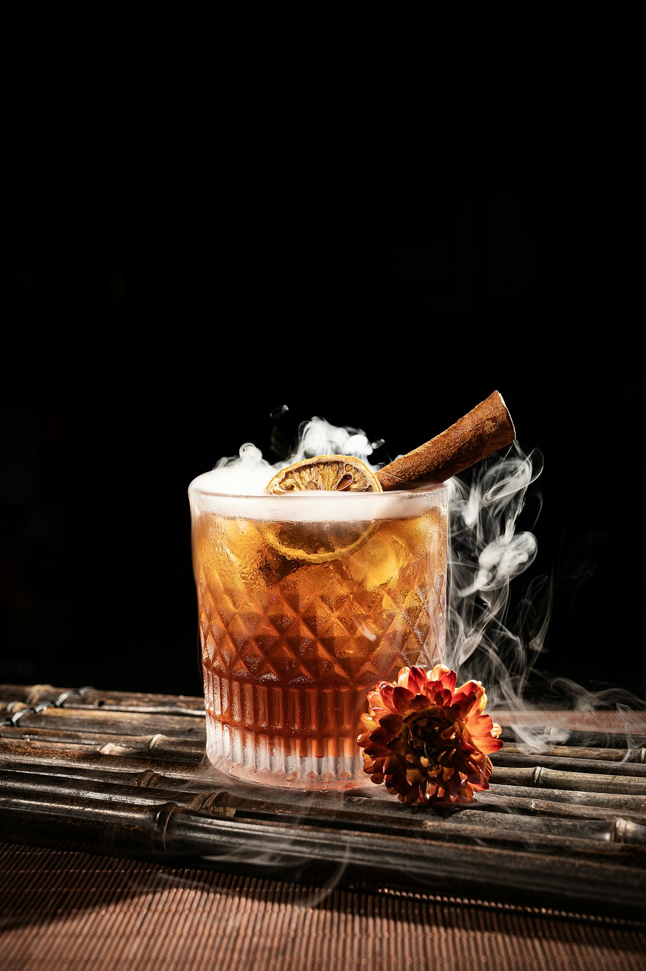 Un cocktail au thé fumé Lapsang Souchong présenté sous une cloche en verre remplie d'une fumée épaisse, révélant une boisson ambrée élégante et créant une ambiance mystérieuse et aromatique.