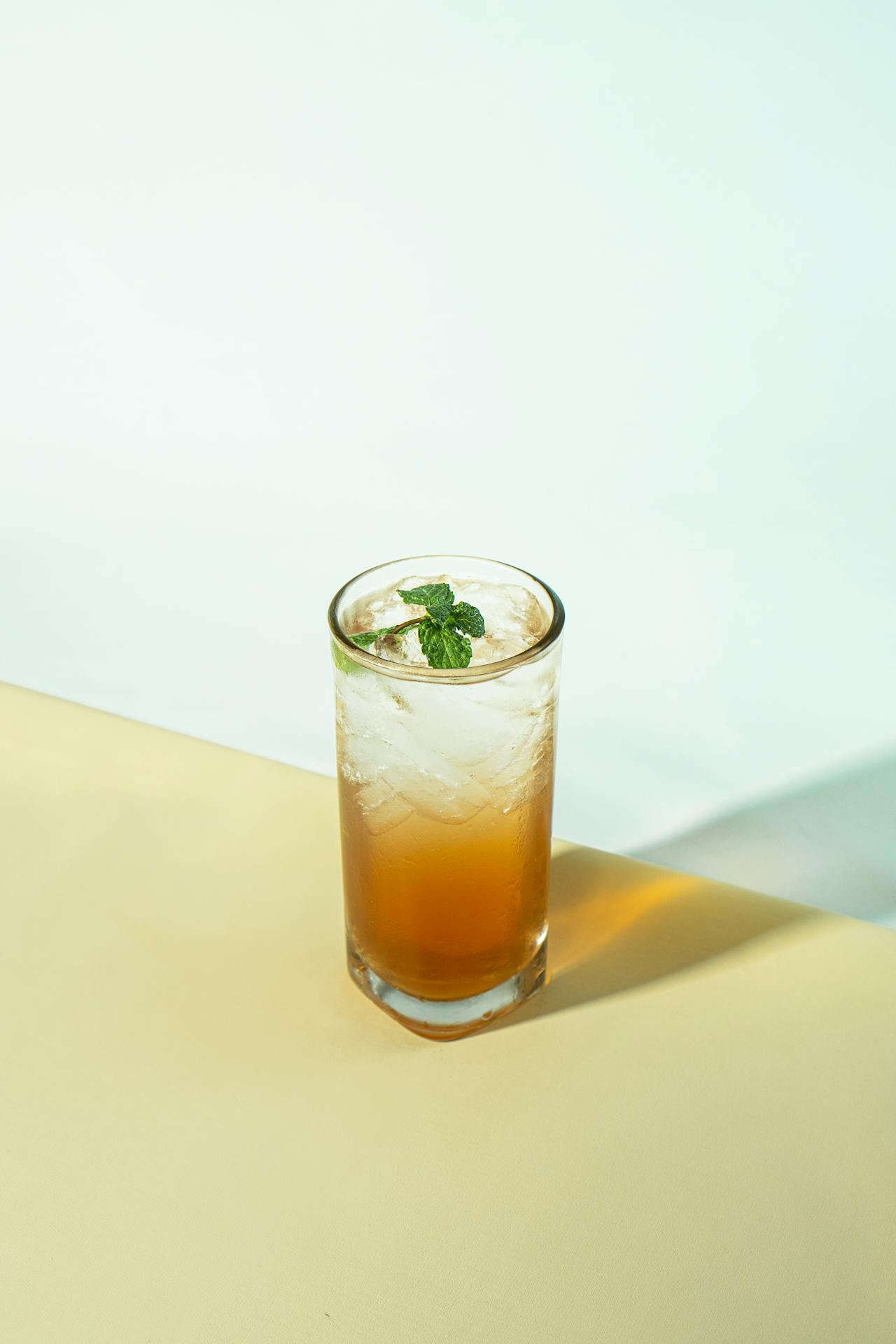 Un verre de cocktail au thé Oolong glacé à la pêche, décoré de fines tranches de pêches fraîches et d'une branche de menthe, posé sur une table en bois ensoleillée.