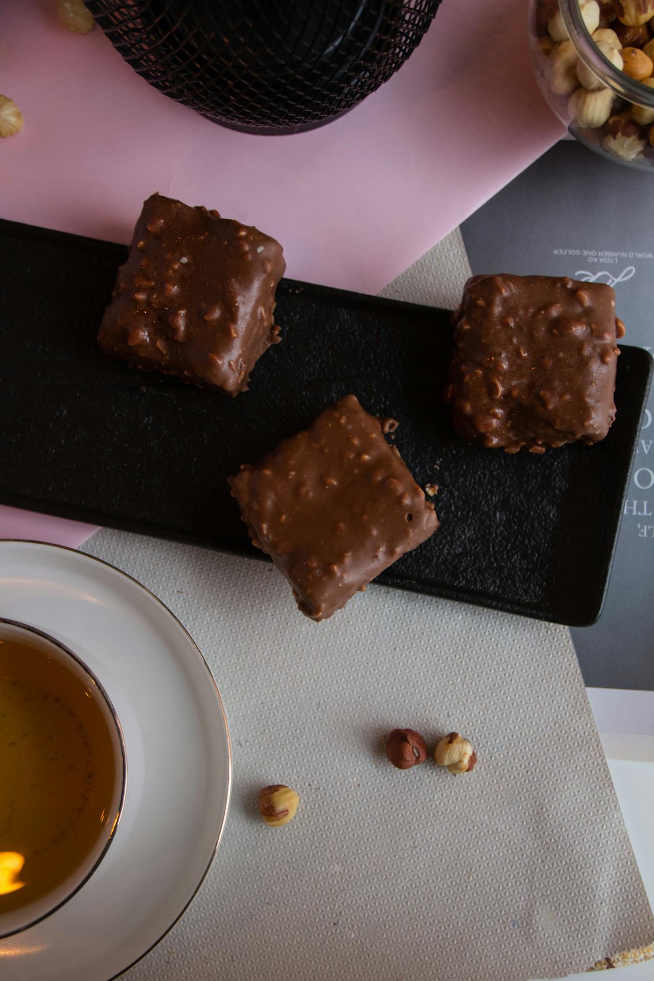 Arrangement gourmand de chocolats pralinés variés et d'une tasse de thé chaud. L'image met en valeur la texture croquante du praliné, idéal pour un accord thé riche et sucré.