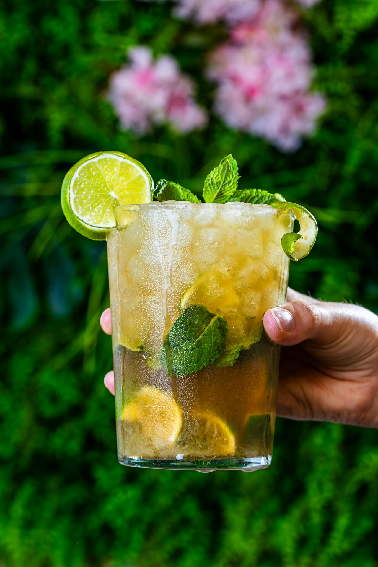 Un cocktail au thé Earl Grey revisité en Mojito, servi dans un grand verre avec beaucoup de glace pilée, des feuilles de menthe fraîche, des quartiers de citron vert et une touche de bergamote sur un fond lumineux.