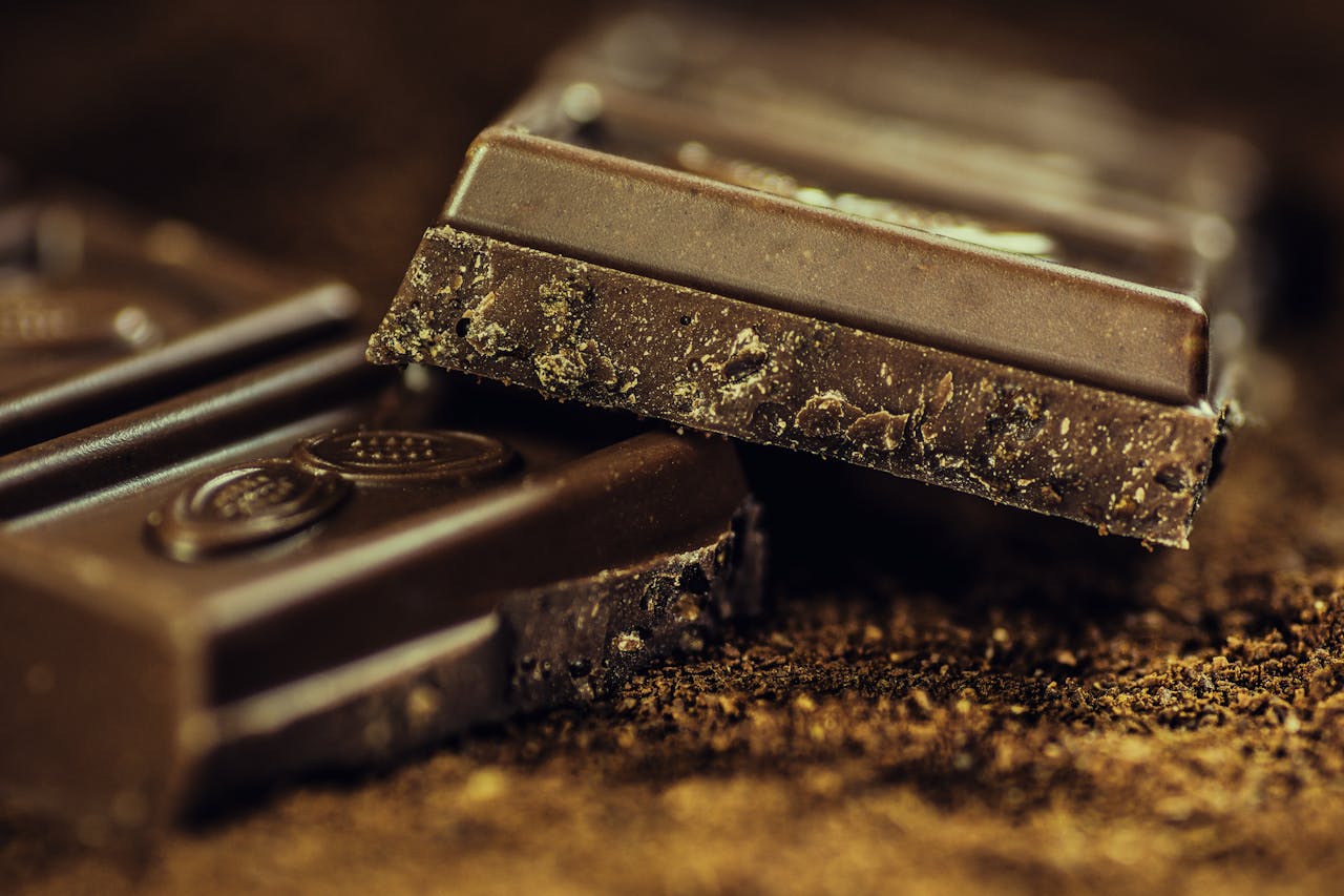 Gros plan sur des carrés de chocolat noir intense (70% ou plus), brillants et lisses. L'image met en valeur la richesse du cacao, idéal pour un accord thé noir corsé.