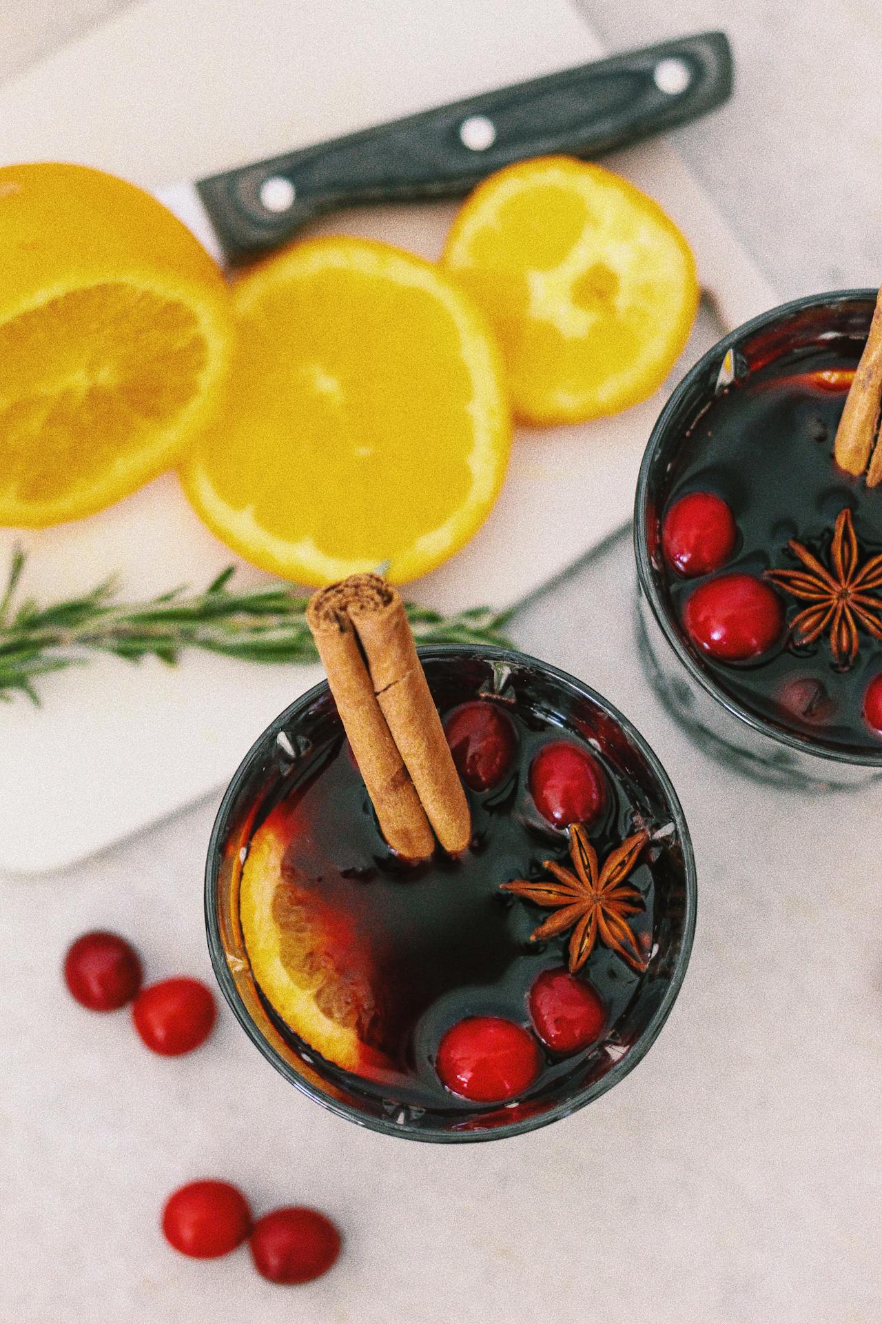 Un grand bol à punch festif rempli d'un cocktail au thé noir et épices de Noël, avec des tranches d'oranges flottantes, des bâtons de cannelle et des étoiles d'anis, entouré de décorations de fêtes et de bougies.