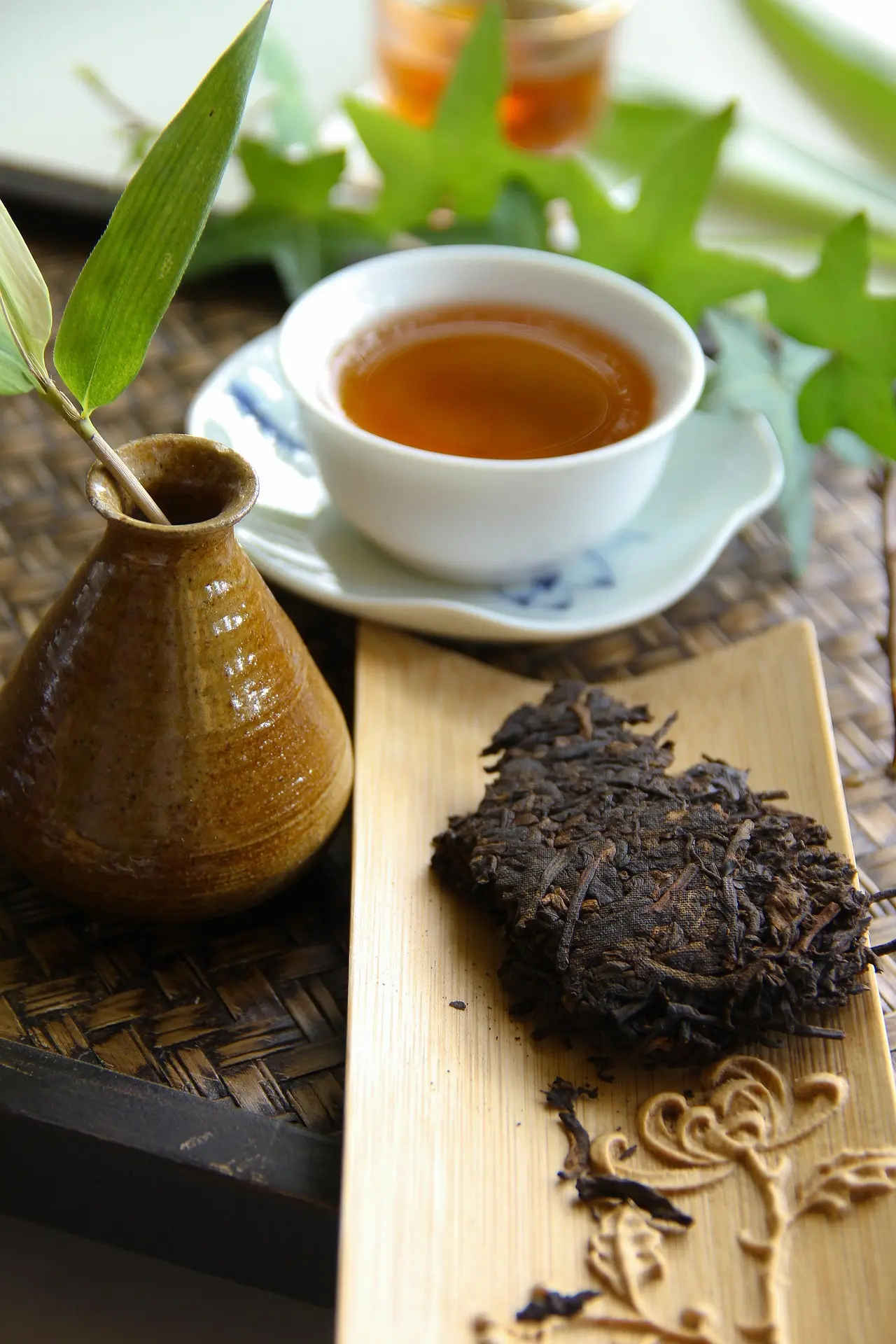 Présentation traditionnelle de thé Pu'er avec une galette compressée et une tasse infusée sur un plateau en bambou. Originaire de Chine, le Pu'er est souvent considéré comme le meilleur thé pour la digestion et est apprécié en France après un repas copieux.