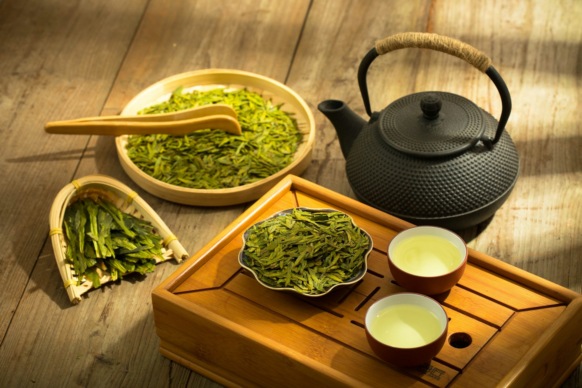 Un service à thé traditionnel en bois avec deux tasses de thé vert infusé, une théière en fonte noire et des feuilles de thé Longjing étalées, illustrant la relation entre la dégustation du thé chinois et la chance dans la culture zen.