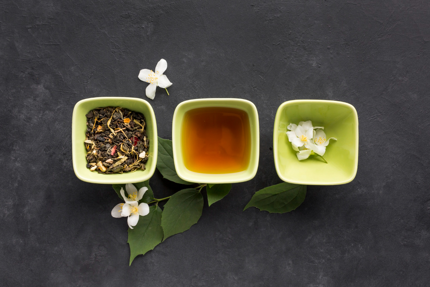 Infusion de feuilles de thé vert et fleurs de jasmin frais dans des bols, illustrant les bienfaits des thés floraux chinois pour la santé et la relaxation.