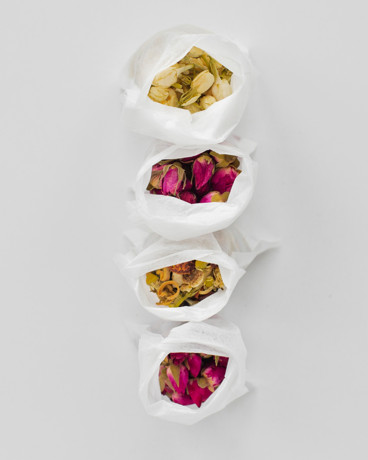 Sélection de fleurs séchées entières pour thé floral : roses, jasmin et camomille présentés dans des filtres individuels pour un mélange de thé de Pâques fait maison.