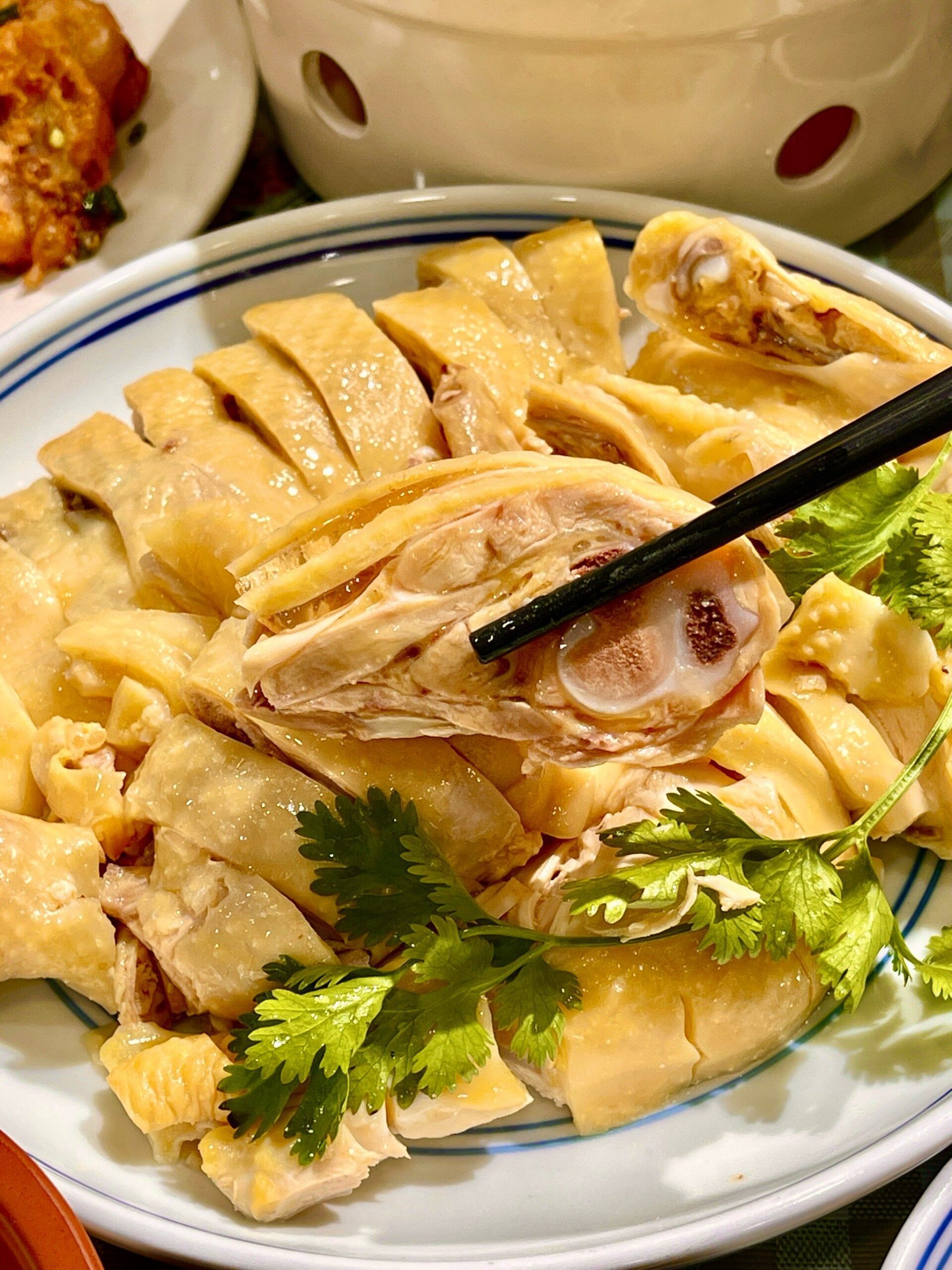 Gros plan sur un poulet de Shanghai découpé de manière traditionnelle, présentant une peau dorée et brillante, agrémenté de feuilles de coriandre fraîche et saisi par des baguettes noires. Ce plat emblématique illustre l'importance des accords thé et plats chinois pour sublimer la finesse des viandes blanches lors d'un repas de fête pour le Nouvel An chinois.