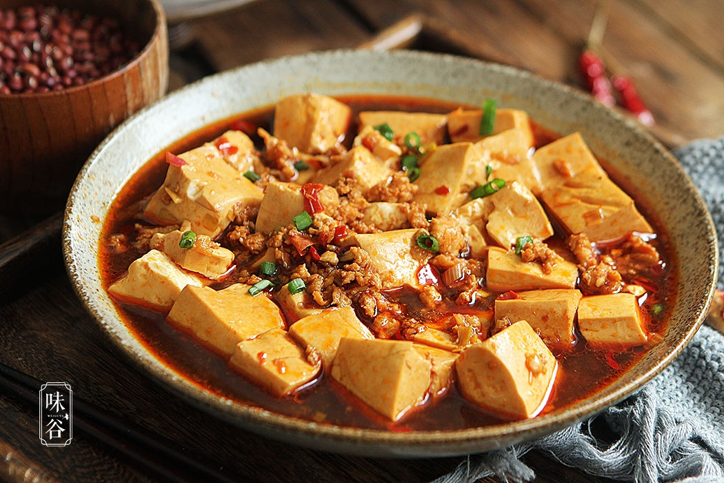 Un plat généreux de Mapo Tofu, composé de cubes de tofu tendres nappés d'une sauce rouge pimentée et agrémentés de viande hachée et d'oignons verts ciselés. Cette recette est un incontournable parmi les plats du Nouvel An chinois pour apporter chaleur et piquant à votre table de fête, idéal à marier avec un thé noir boisé.