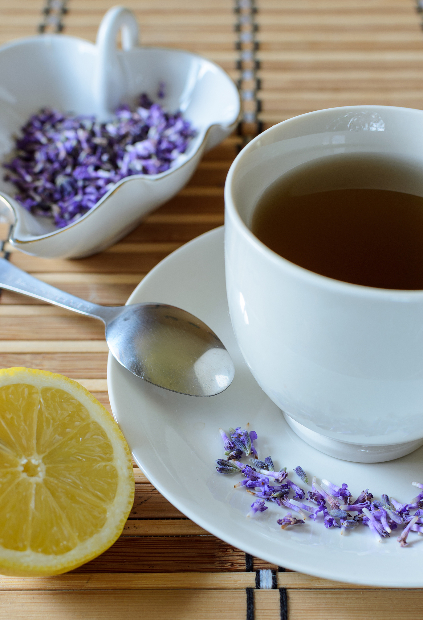 Un thé aux fleurs de lavande d'un violet profond, infusé dans une tasse et une théière en verre transparentes, entourées de brins de lavande fraîche sur une table en bois.