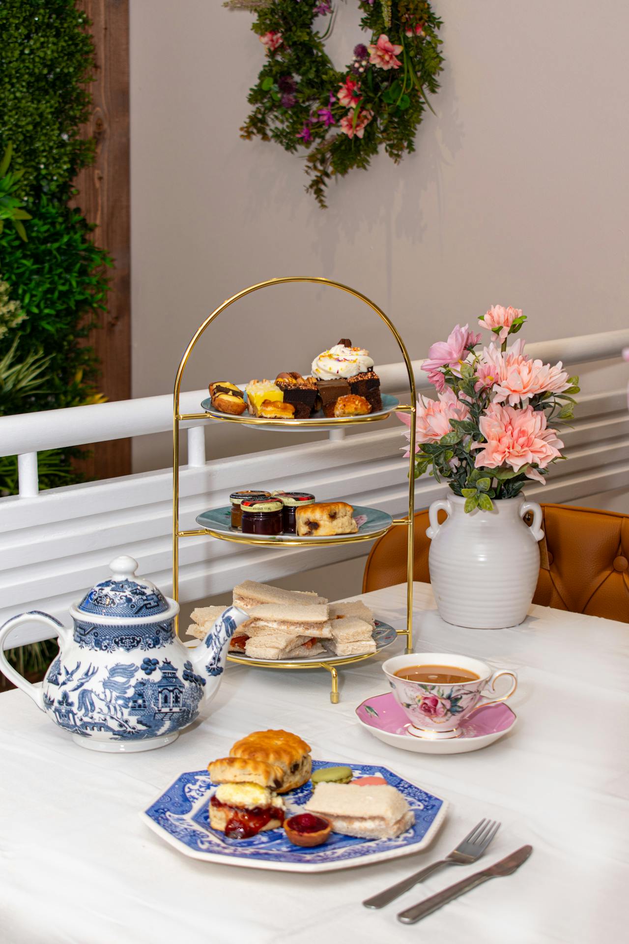 Mise en scène d'un goûter de Pâques raffiné : présentoir à étages rempli de mignardises, service à thé vintage en porcelaine fleurie et bouquet printanier sur une nappe blanche lumineuse.