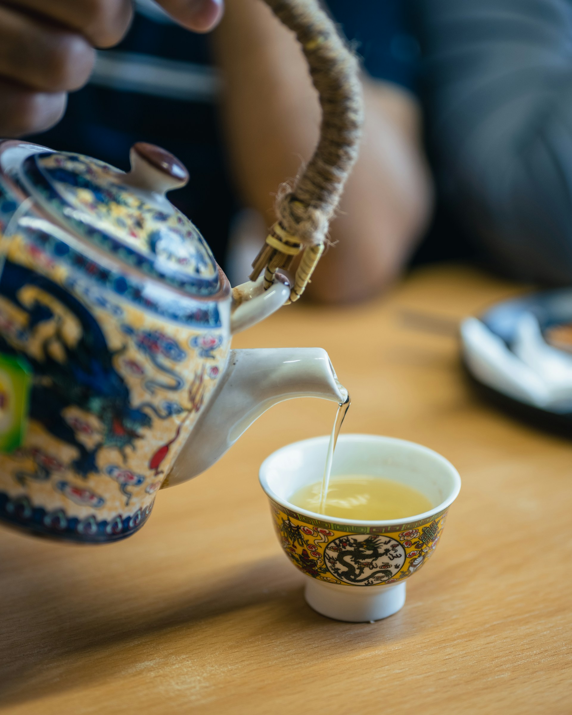 Gros plan sur une théière traditionnelle asiatique versant un thé oolong dans une tasse assortie. Ce visuel illustre la différence théine et caféine, la première offrant une stimulation plus douce et durable que le café.