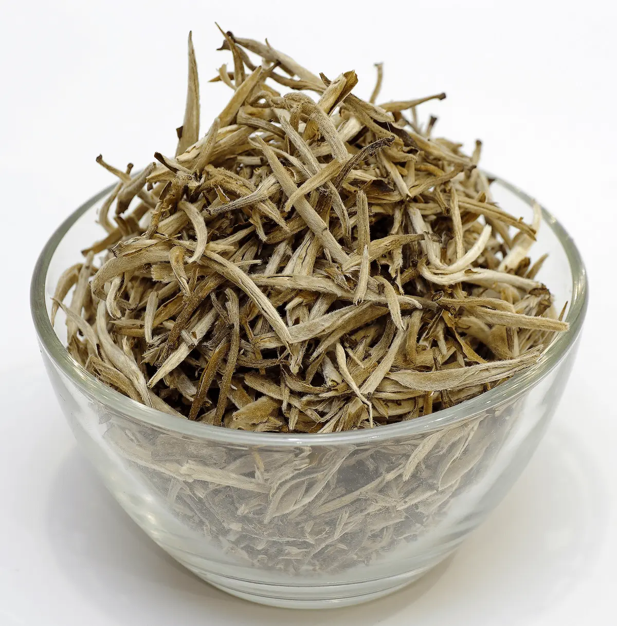 Un bol en verre rempli de feuilles de thé blanc chinois en vrac, mettant en valeur leur couleur claire et leur structure délicate.