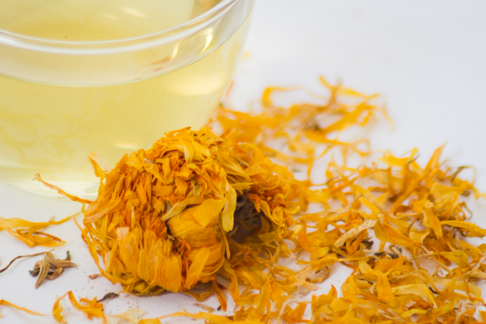 Fleurs de chrysanthèmes séchées et leur infusion dorée dans une tasse, une infusion sans théine soir parfaite pour apaiser la fatigue oculaire et se détendre.