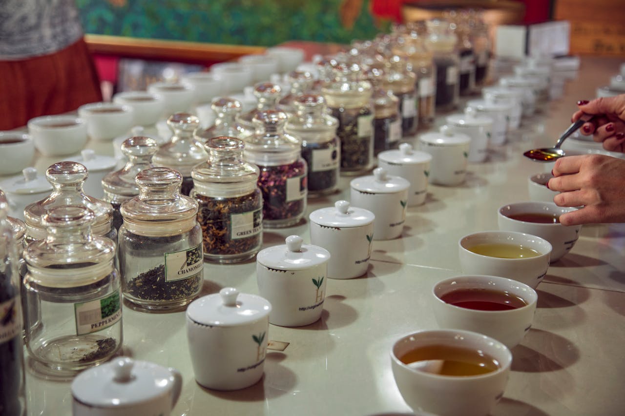 Une rangée de tasses professionnelles et de pots de feuilles sèches utilisée pour une dégustation du thé comparative, permettant d'enrichir son vocabulaire du thé et de maîtriser comment décrire un thé en analysant le profil aromatique du thé et en rédigeant des notes de dégustation détaillées.