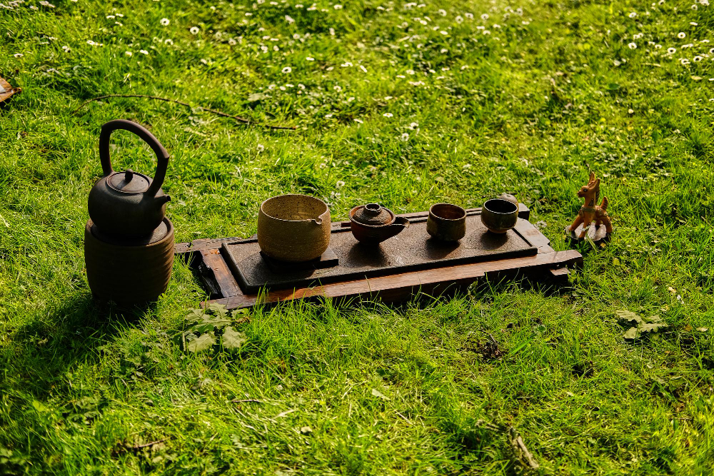 Service à thé en argile disposé sur l'herbe pour une cérémonie de thé nomade. Théière et petites tasses invitent à boire du thé en voyage en pleine conscience, au contact de la nature.
