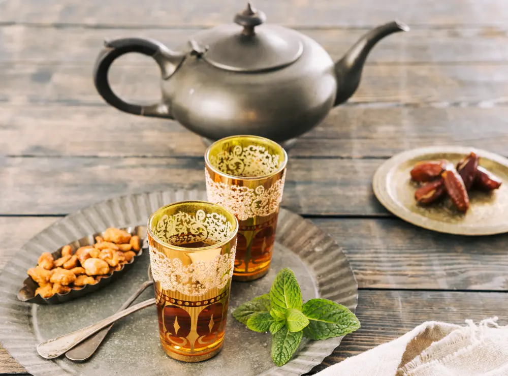 Tasses en verre de thé vert à la menthe, meileur thé pour l'été sur une table. Dessus sont posés une théière en fer et des dattes.