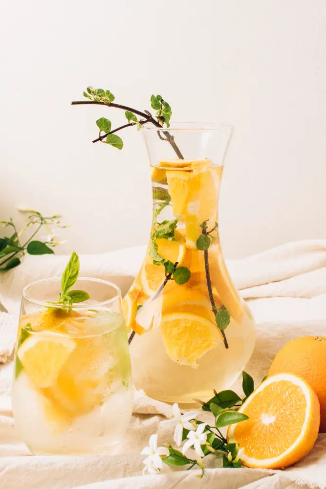 Une carafe et un verre de thé jasmin glacé aux fruits frais fait maison aux rondelles d'orange et de citron avec des feuilles de menthe pour se désaltérer.