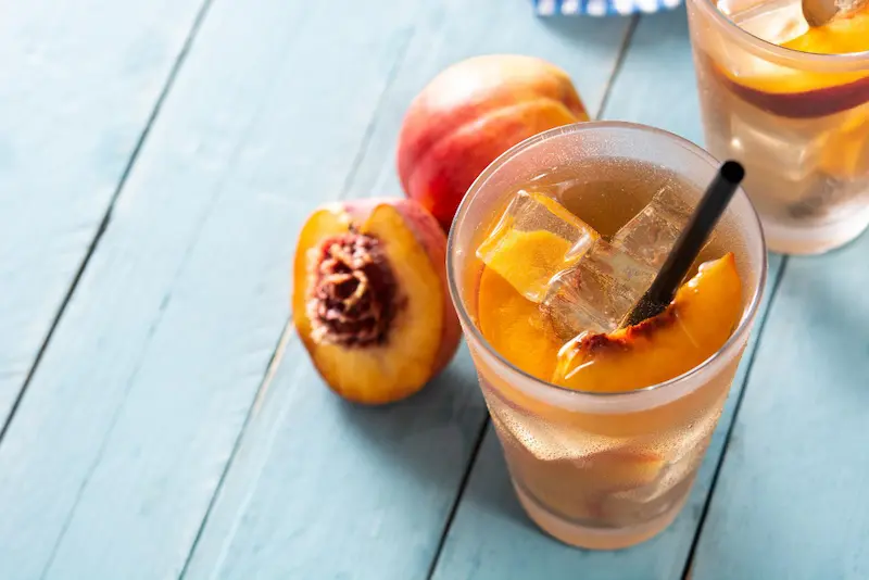 Un verre de thé oolong pêche glacé à la pêche avec des glaçons et une paille, posé sur une table en bois bleu, idéal comme l'un des meilleurs thés fruités pour l'été.