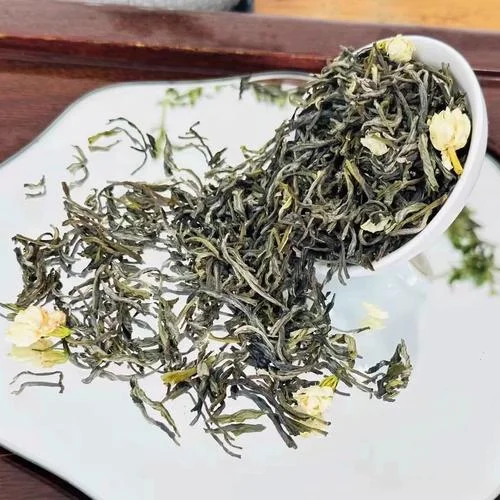 Gros plan sur du thé vert en vrac mélangé à des fleurs de jasmin séchées, illustrant le processus traditionnel de parfumage où les feuilles de thé absorbent naturellement le parfum des fleurs fraîches.