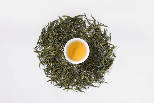 Petite tasse de thé vert entourée de feuilles de thé vert