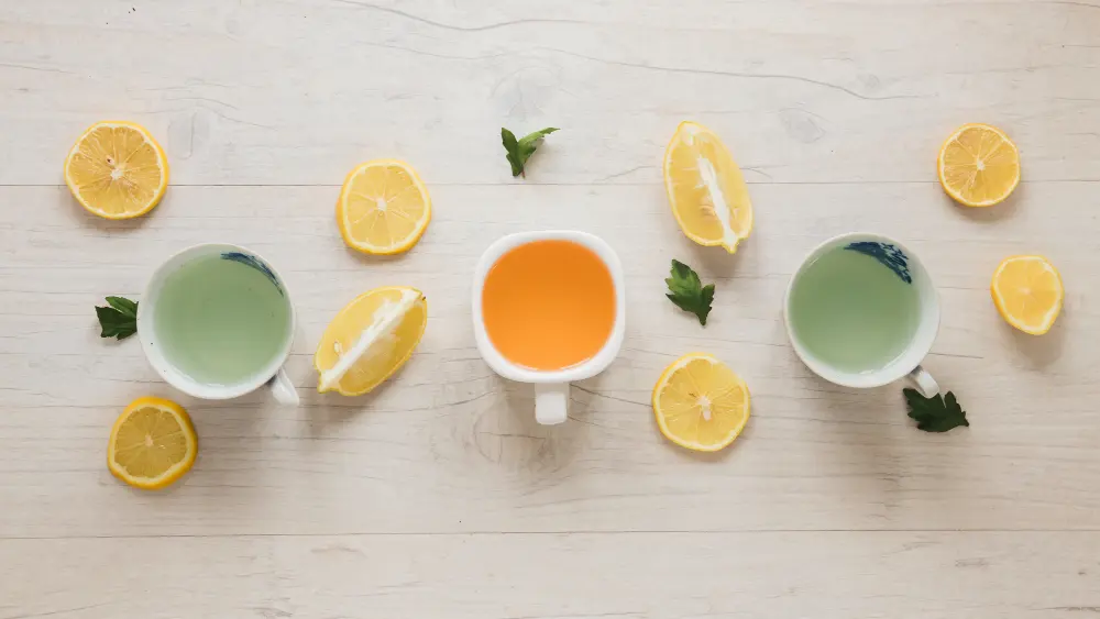 Vue du dessus de tasses de thé vert chinois entourées de rondelles de citron frais, parfait pour savoir quel thé boire le matin pour un réveil énergétique et anti-nausée.