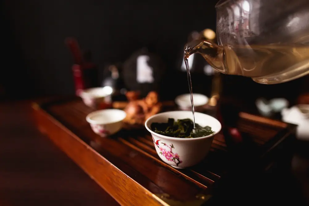 Infusion de feuilles de thé de Chine dans un bol en porcelaine fleurie sur un plateau de dégustation, idéal pour illustrer quel thé boire le matin.   
