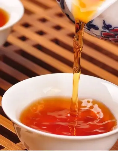 Thé Keemun ambré versé depuis une théière chinoise dans une tasse blanche en céramique