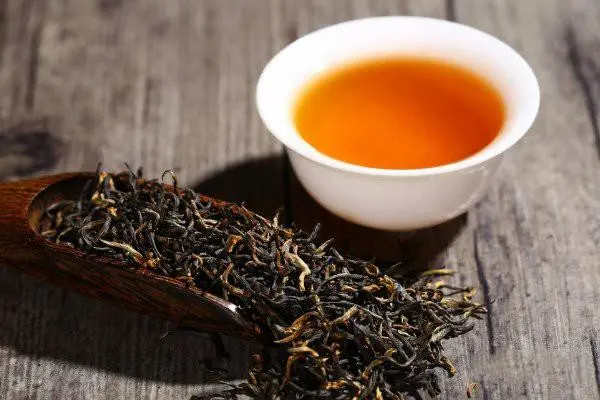 Feuilles de thé noir Keemun sèches à côté d’une tasse d’infusion ambrée