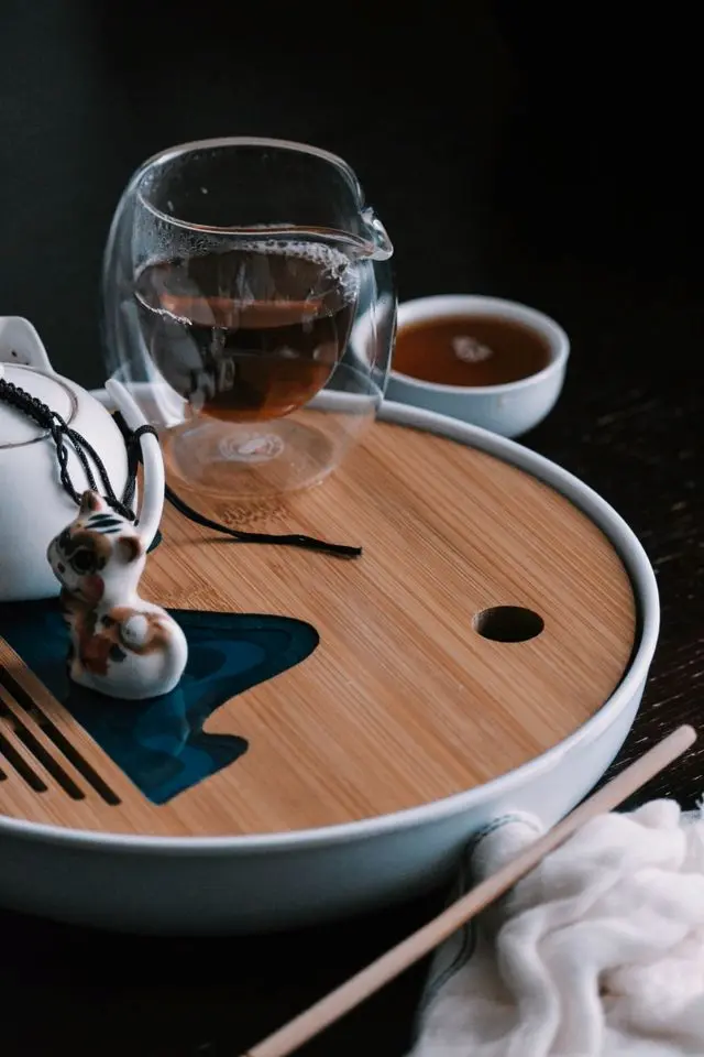 Infusion de thé pu-erh dans un pichet en verre sur un plateau à thé traditionnel en bambou avec un tea pet et une théière en céramique.