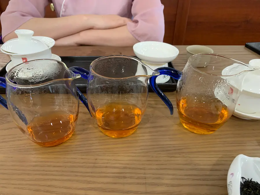 Trois pichets en verre révélant les nuances ambrées de la liqueur lors d'une dégustation de thé keemun pendant un voyage à Qimen.