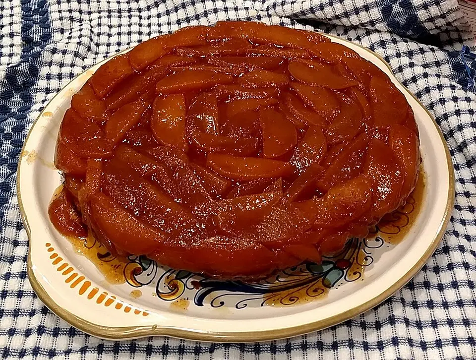 Une tarte Tatin aux pommes généreusement caramélisées, présentée sur un plat décoré pour un moment thé et dessert d'automne réconfortant.